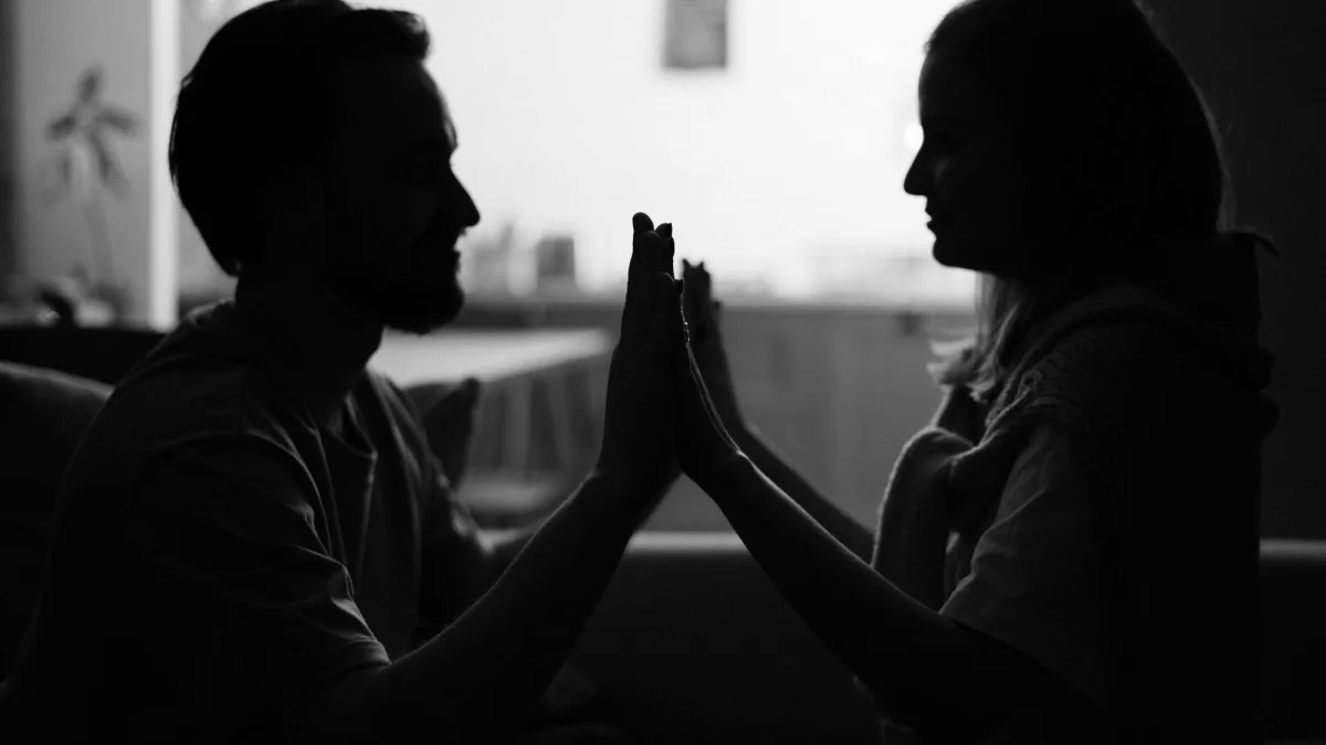 Silhouette eines Paares, das sich im warmen Dämmerlicht die Handflächen berührt, als Sinnbild für Nähe und nachlassende Lust in der Beziehung